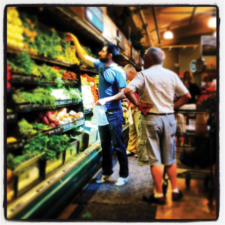 An oily photo of a man reaching for some sort of vegetable on a store shelf. Others around him do the same.